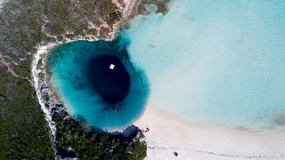 aerial image showing a huge blue sinkhole in the Caribbean with a white sandy beach and blue sea