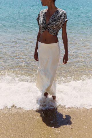 Woman on beach wears blue top and white slip skirt