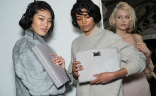 three female models wearing cosy grey jumpers and holding grey handbags