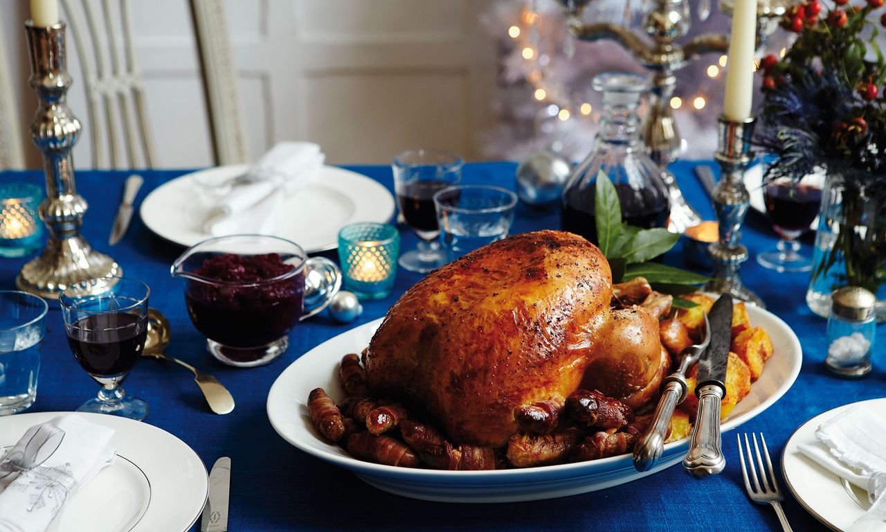 dinner table with blue tablecloth and turkey and dinner platters and candle