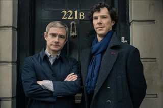 Martin Freeman and Benedict Cumberbatch stand outside of a door labeled 221 b in a still from Sherlock