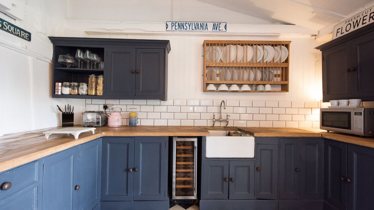 An image of a kitchen with white tiled walls, blue cabinets and wooden countertops