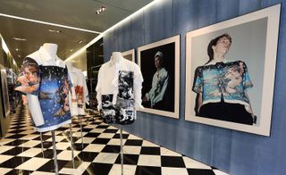 Male torso mannequins with button up shirts with images printed on them on a black and white checkered floor and large photographs in frames on the walls.