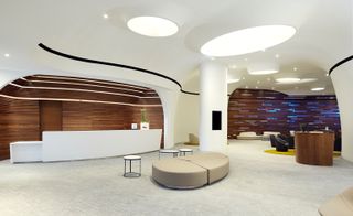 Reception area of the Double Tree by Hilton hotel in Poland with white reception desk, walls and ceiling, grey tiled floor and beige seating