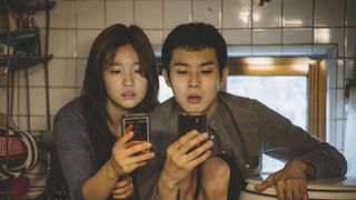 a brother and sister sit on their phones in a tight bathroom space in a still from parasite