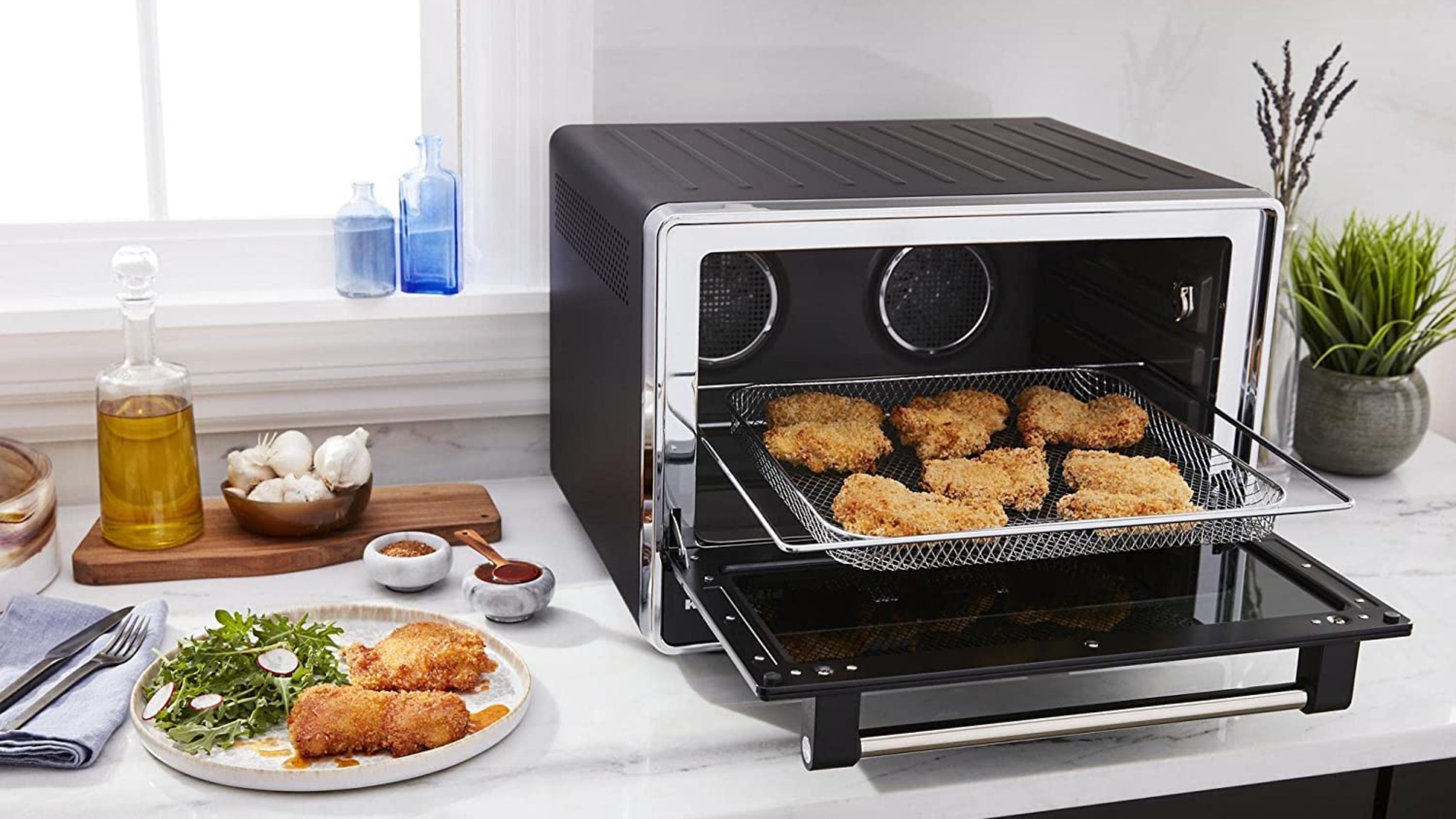 The KitchenAid countertop oven air frying chicken on the surface with food to the left hand side