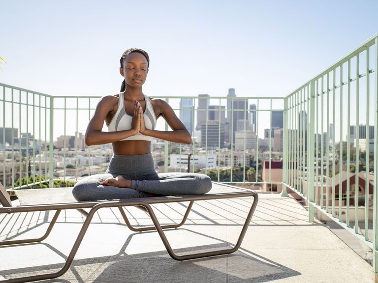 Young woman meditating with city in background, best meditation apps