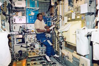 Astronaut Michael P. Anderson inside the Columbia space shuttle holding a large binder list.