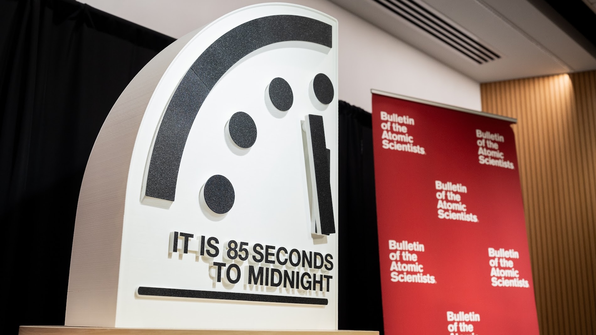 A presentation showing part of a clock at 85 seconds to midnight next to a red banner of the Bulletin of the Atomic Scientists. 