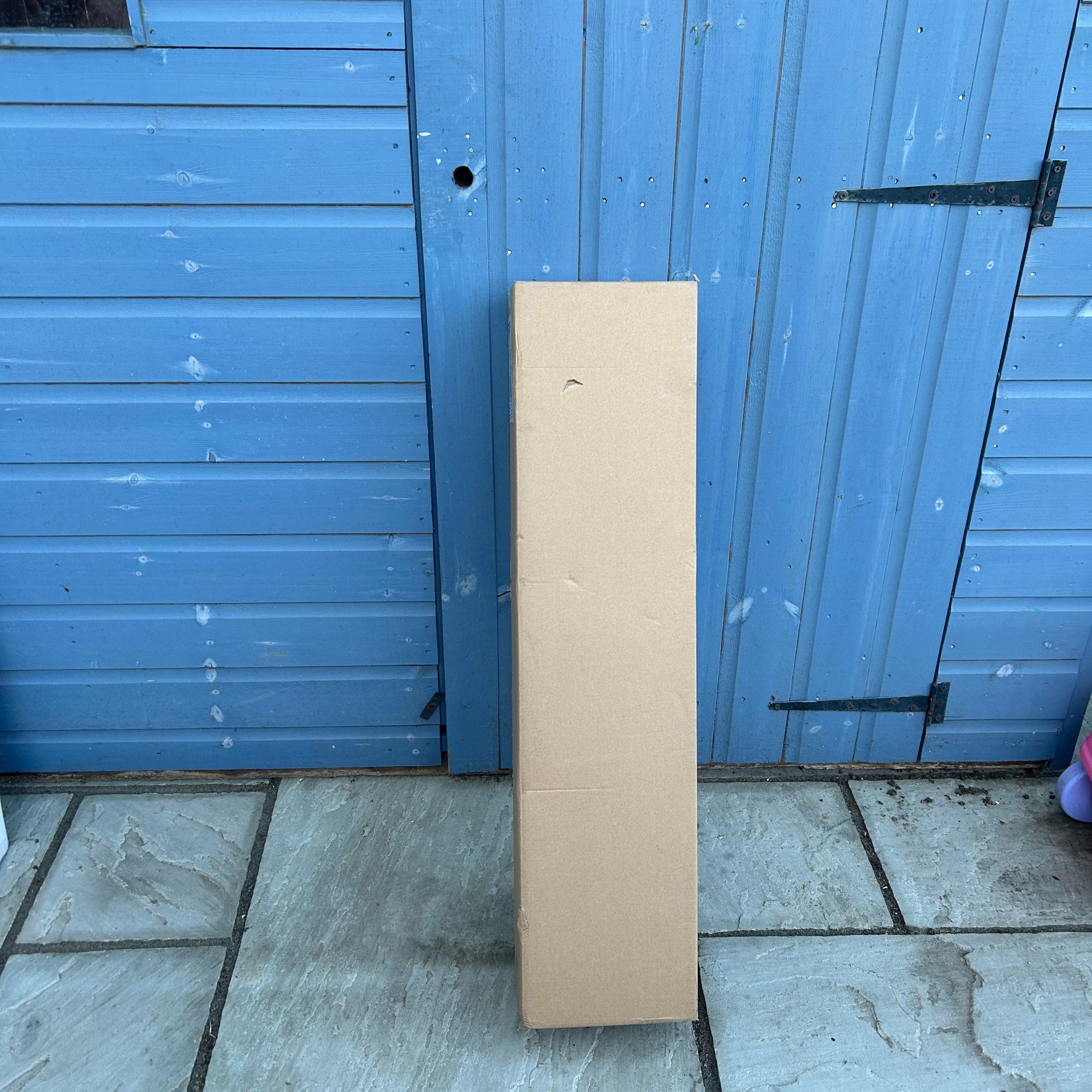 VonHaus G-Series Cordless Grass Trimmer in box, leaning on blue shed