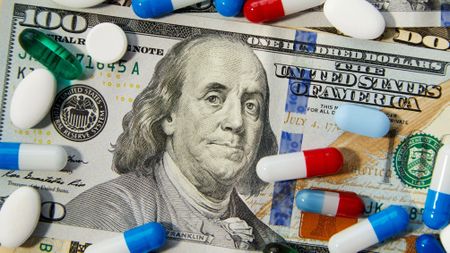 Close-up shot of different sized prescription pills spilled on a background of US dollars