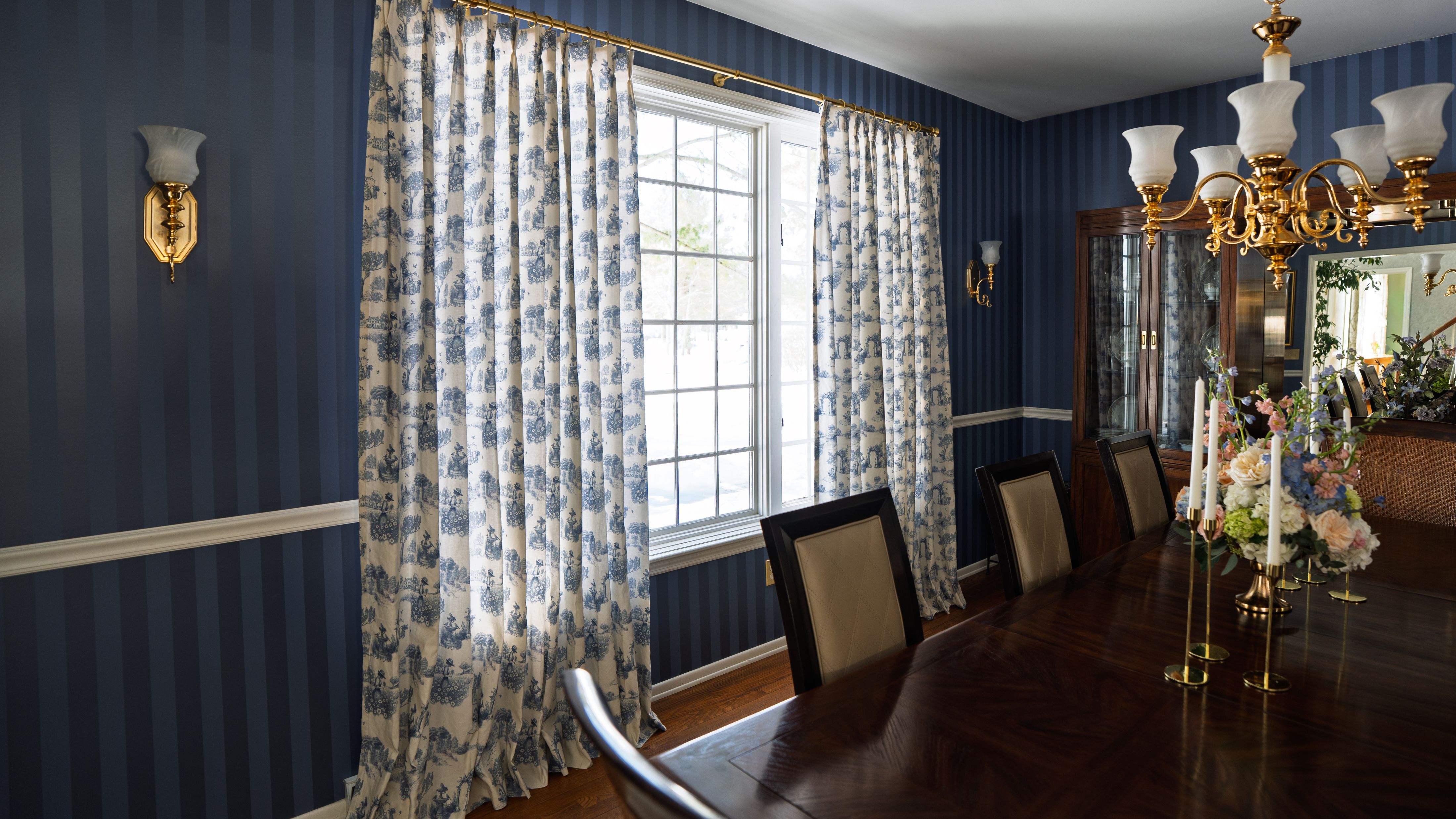 Retro dining room featuring opulent dining furniture, brass wall sconces, and toile de jouy patterned curtains