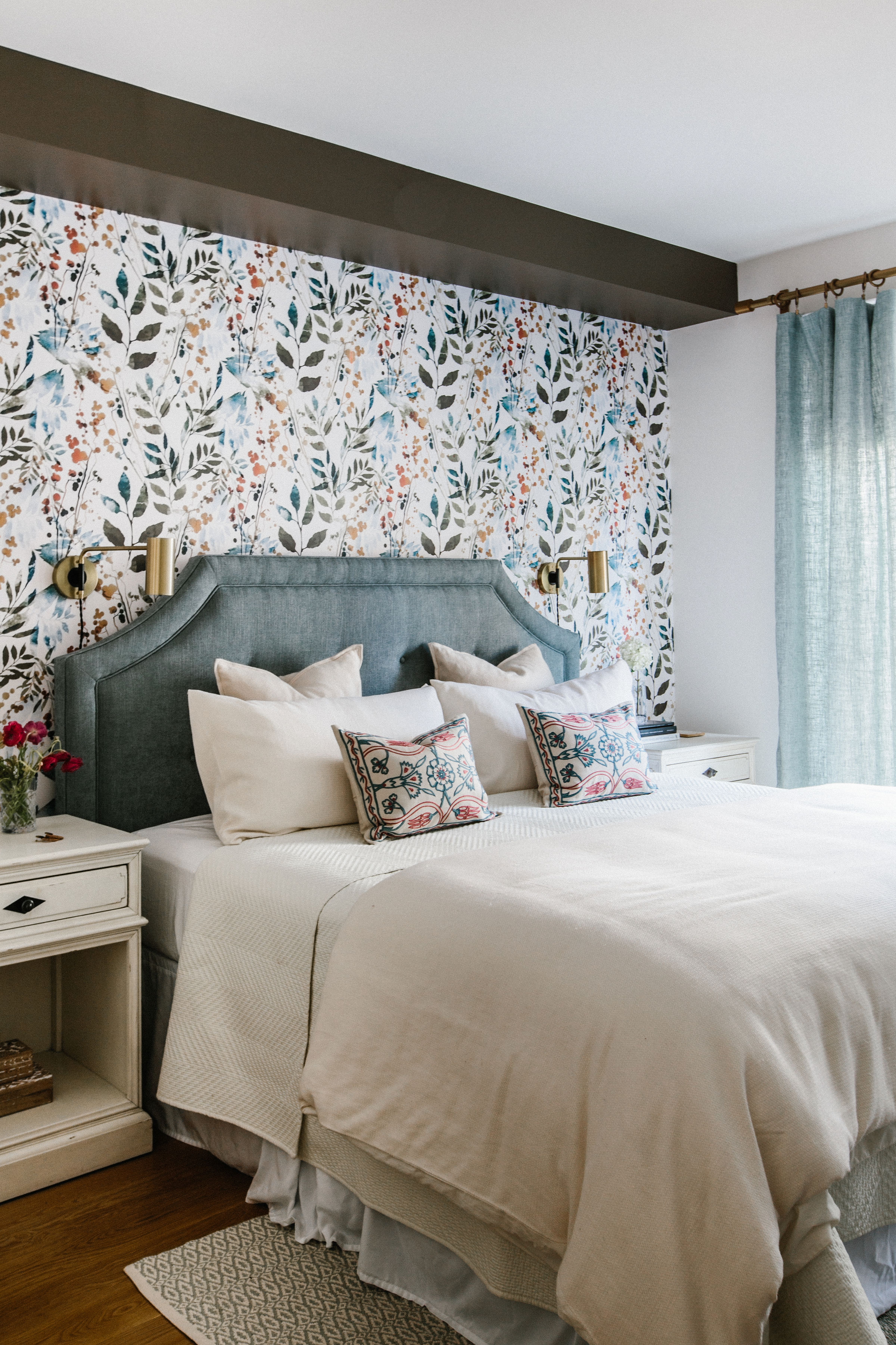 The best bedroom colors with cream, blue and orange woven into a light scheme with cream bedlinen and bedside tables, a duck egg blue headboard and delicately patterned wallpaper.