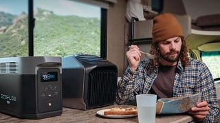 A man sitting in his converted van eats a meal whilst a EcoFlow Delta Max 2000 generator sits on the table