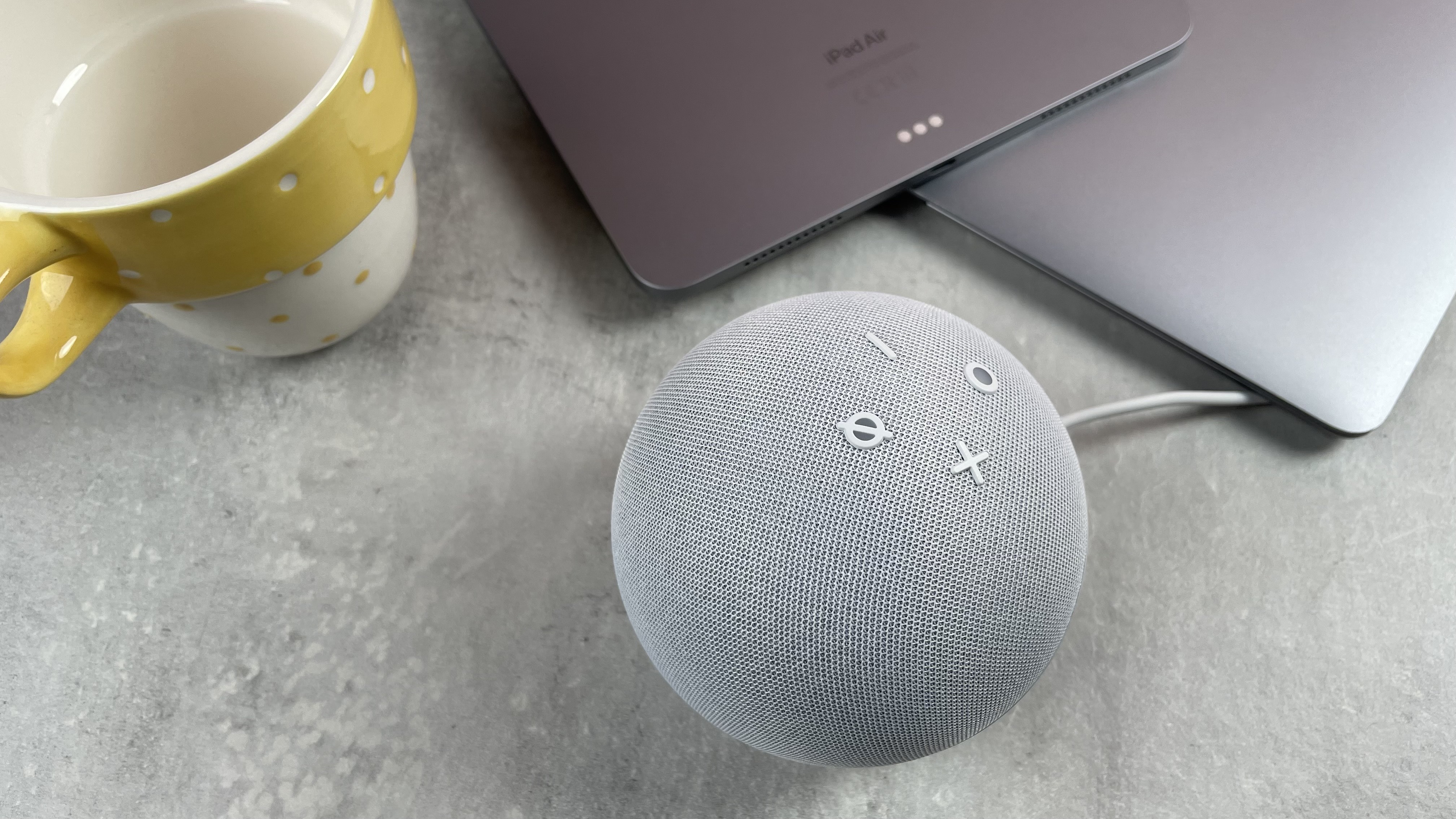 The Echo Dot is pictured in front of an iPad and MacBook on a desktop.