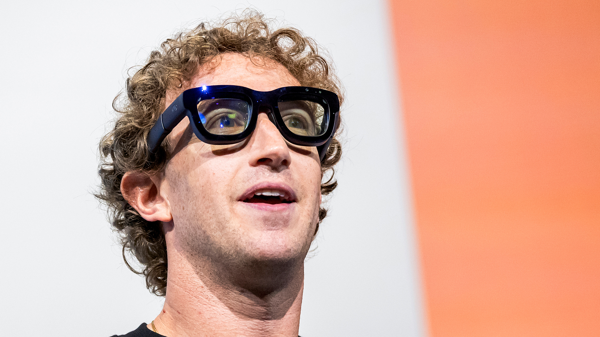 A telephoto shot of Mark Zuckerberg, CEO at Meta, wearing Orion augmented reality (AR) glasses during the Meta Connect event in Menlo Park, California. He is set against an orange and white background.