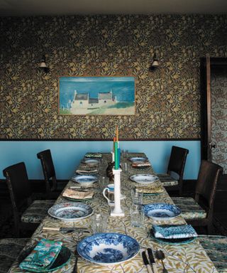 Dining room with william morris wallpaper and blue painted walls, dining table with floral tablecloth and accessories