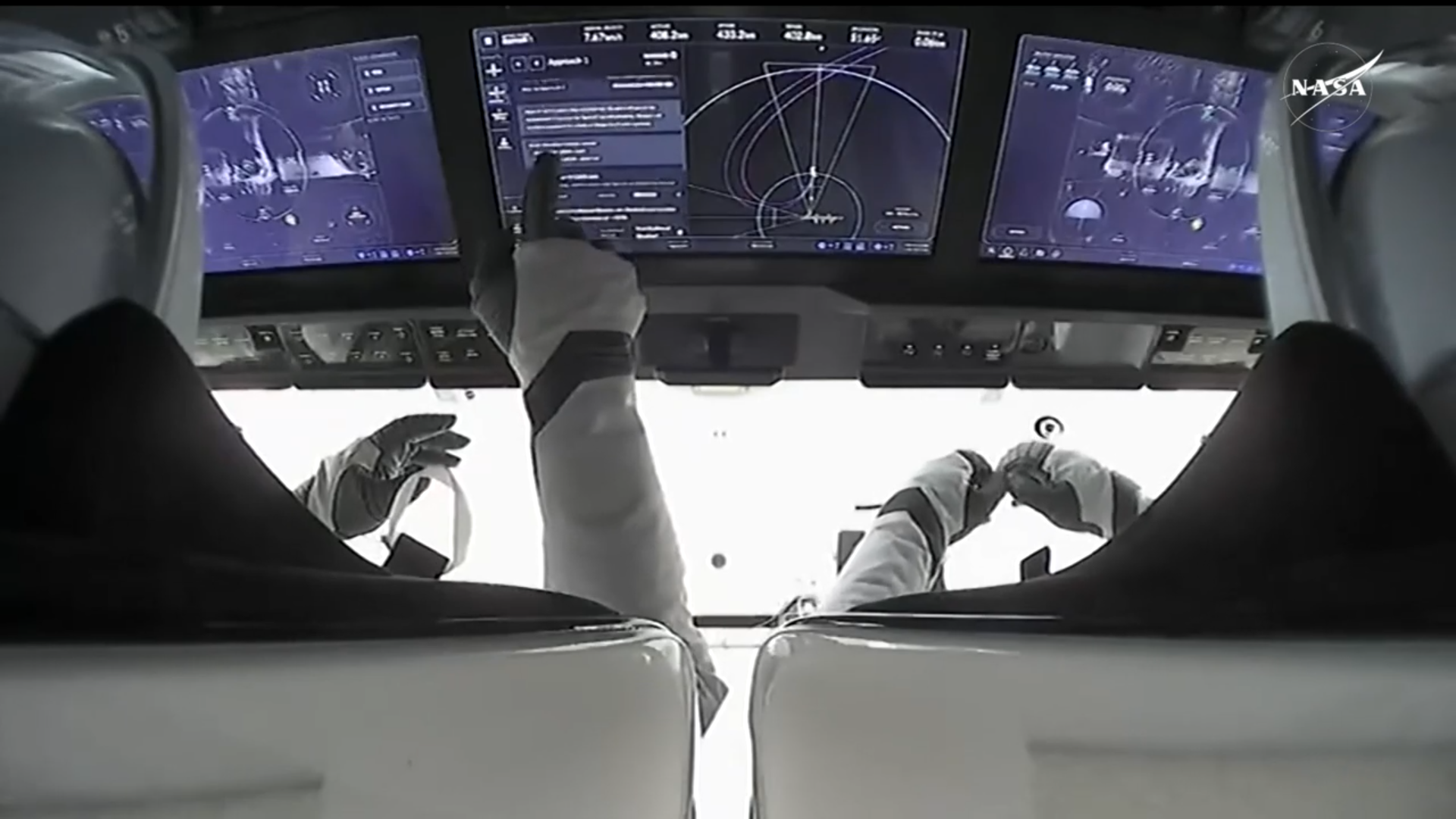 Two astronauts work working on blue computer touch screens to control their SpaceX Dragon capsule.