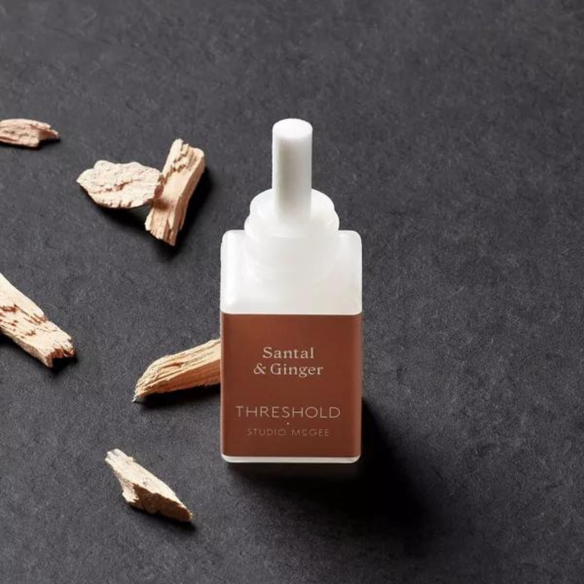 A small Pura fragrance bottle surrounded by shards of wood