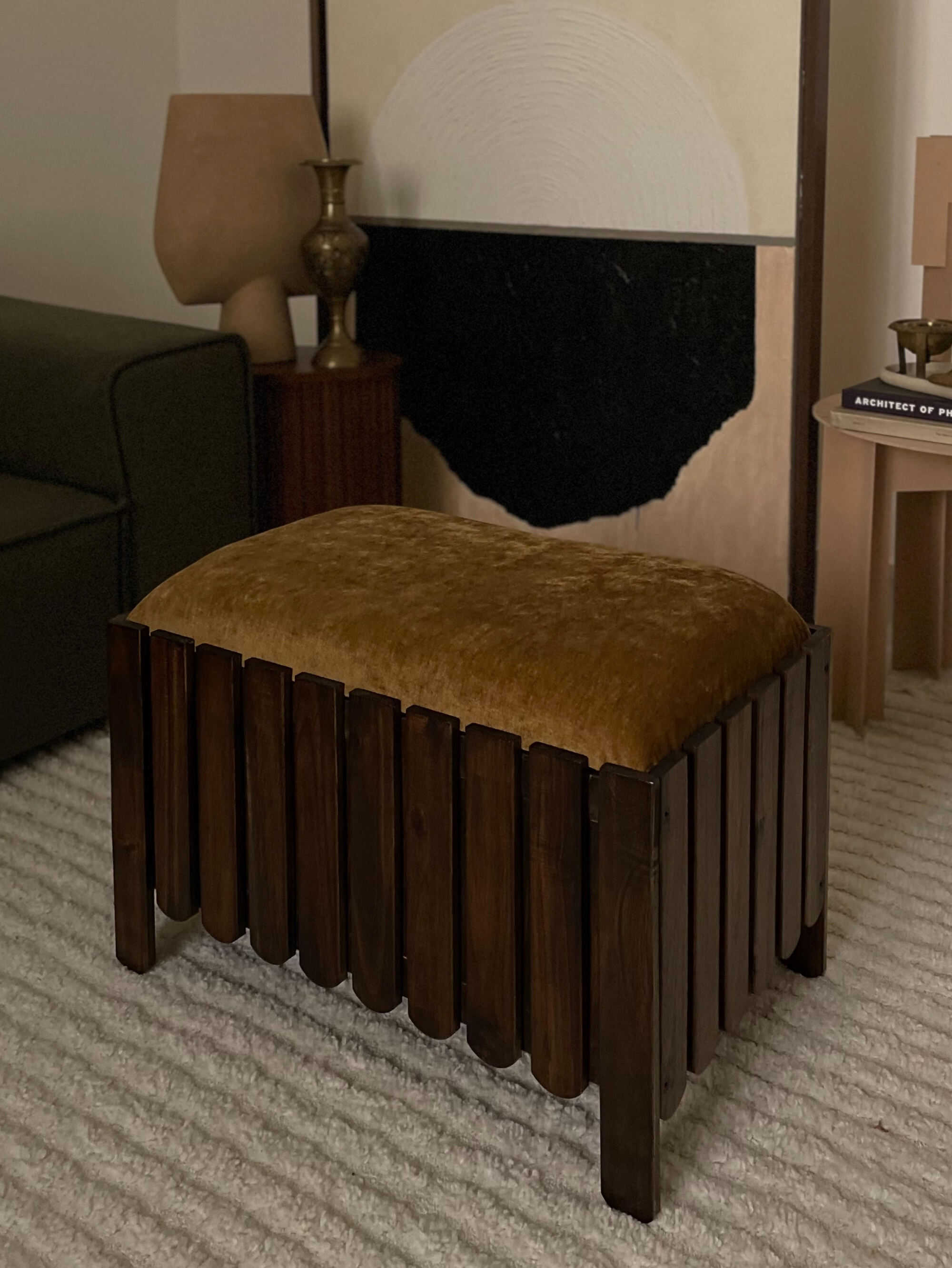 A dark wooden flower box with scalloped edges that has been turned into a stool/ottoman. The cushion on top is an ochre yellow fabric. 