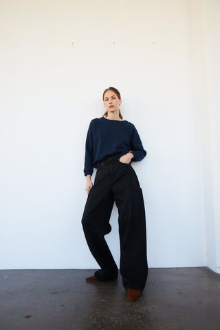 a model stands in front of a white wall wearing a sweater with barrel leg jeans and loafers