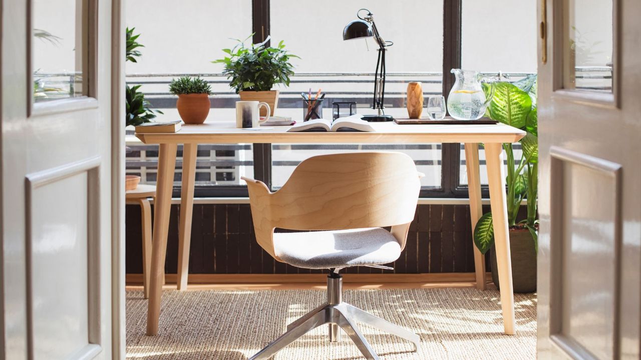 A desk with computer, lamp, and plant with a swivel chair 