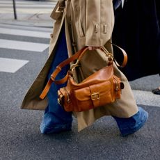 Person in wide-leg jeans, a trench coat, and boots walking in the street holding a leather handbag