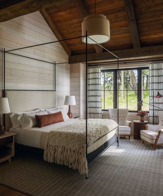 Black four poster bed, white armchairs, wooden ceiling