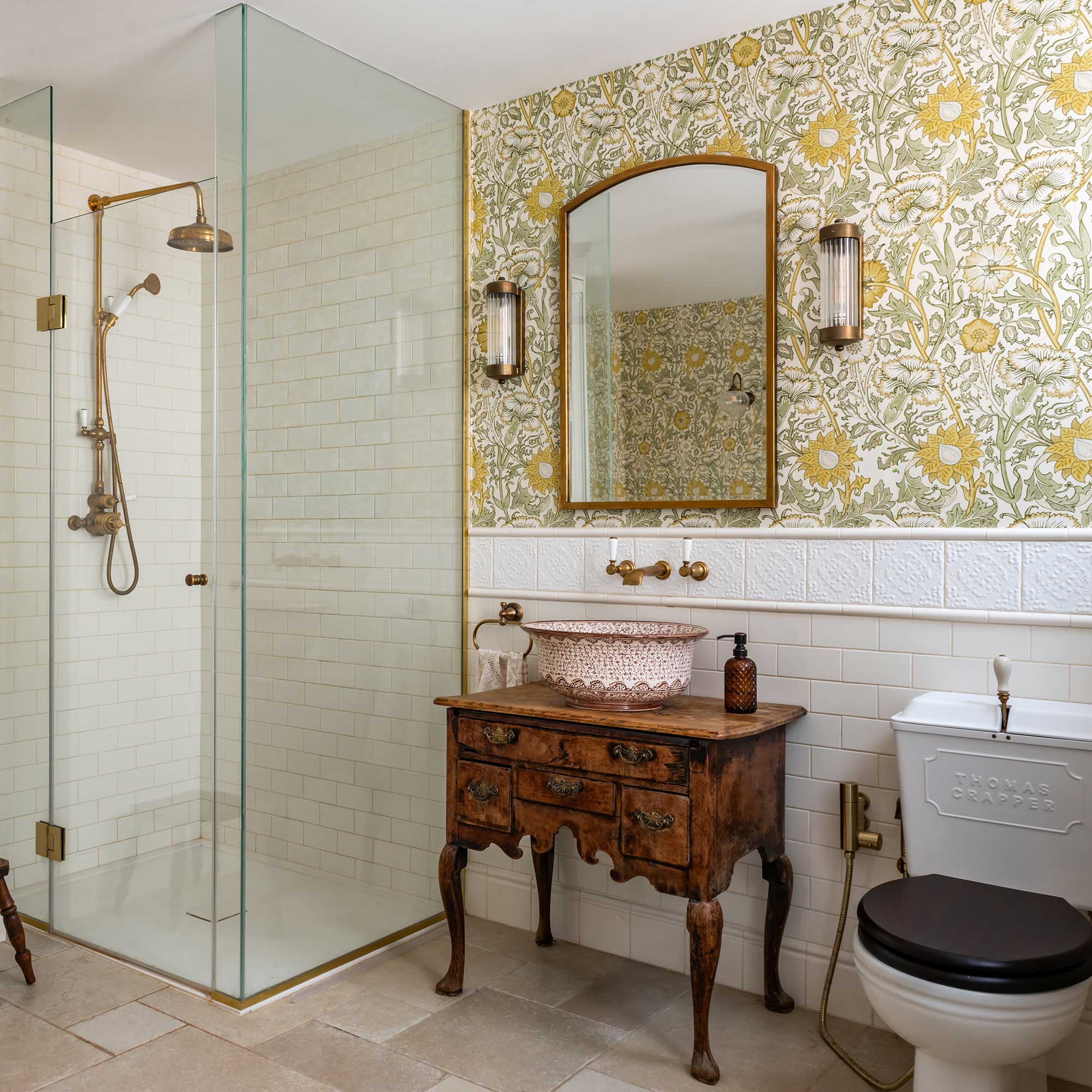 bathroom with antique upcycled vanity stand, brass sanitaryware, wallpapered walls, glass shower unit