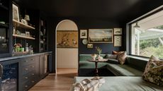 Living room with dark blue painted walls and ceiling, sage green velvet banquette seating and built-in bar