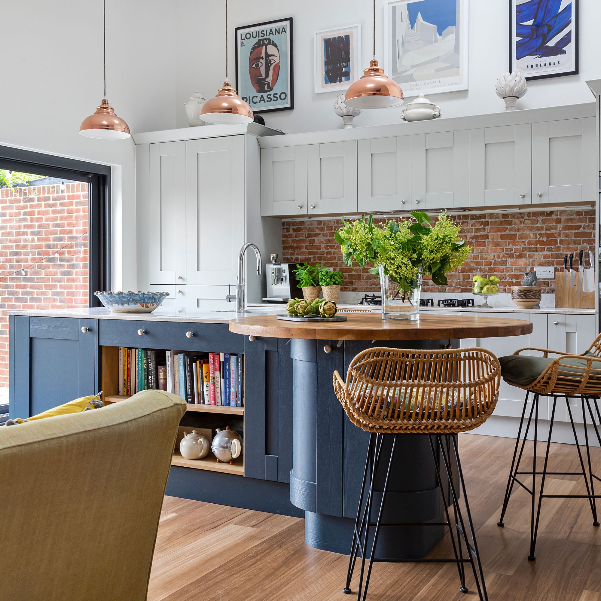 Shaker-style kitchen with a mix of gray and navy cabinets, white round island and rattan style chairs with copper lighting
