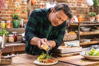 Jamie Oliver grates cheese over a hot dish of something tasty looking.