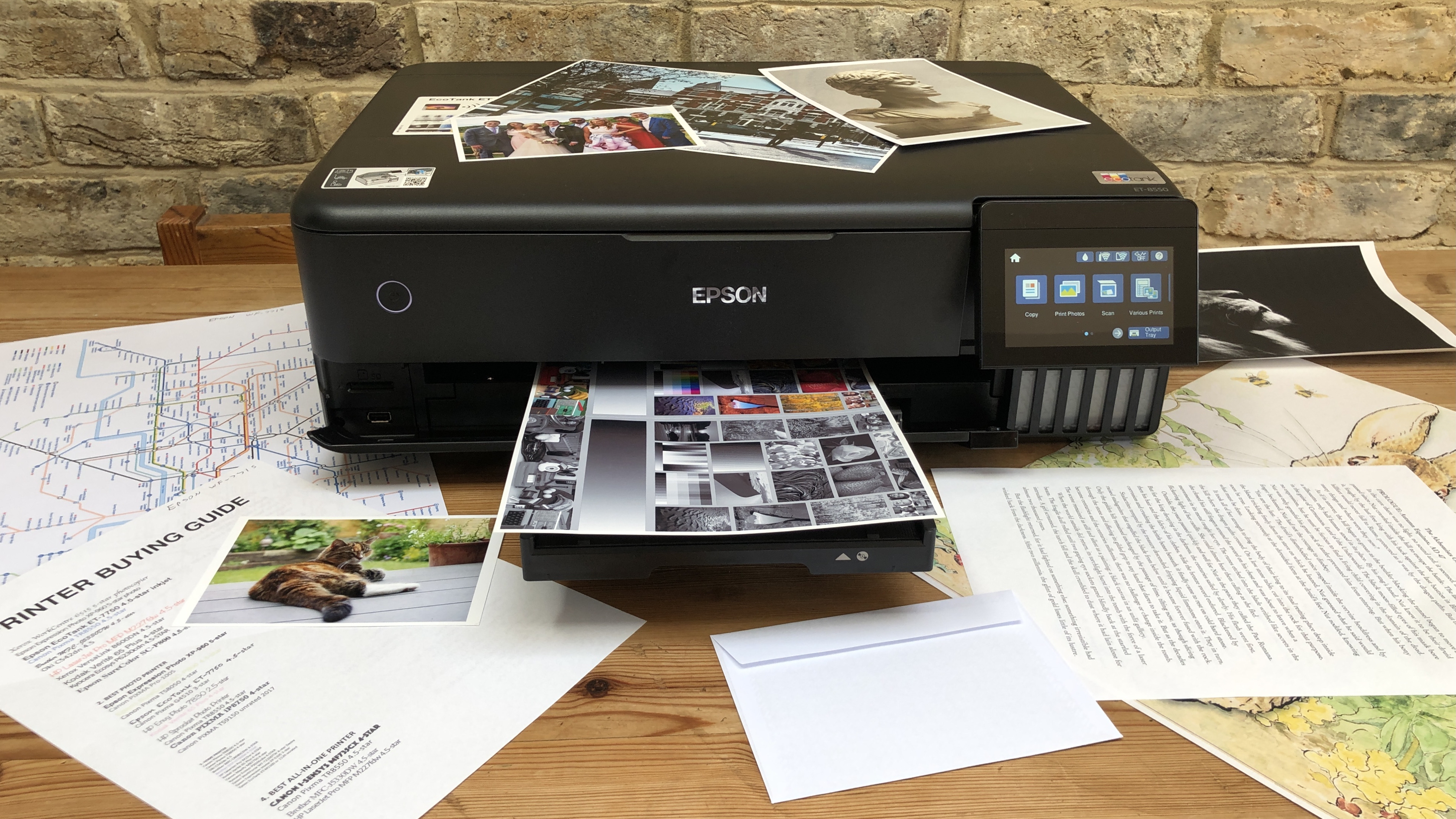 En svart Epson EcoTank ET-8550 står på ett träfärgat bord täckt med papper och utskrivna fotografier.