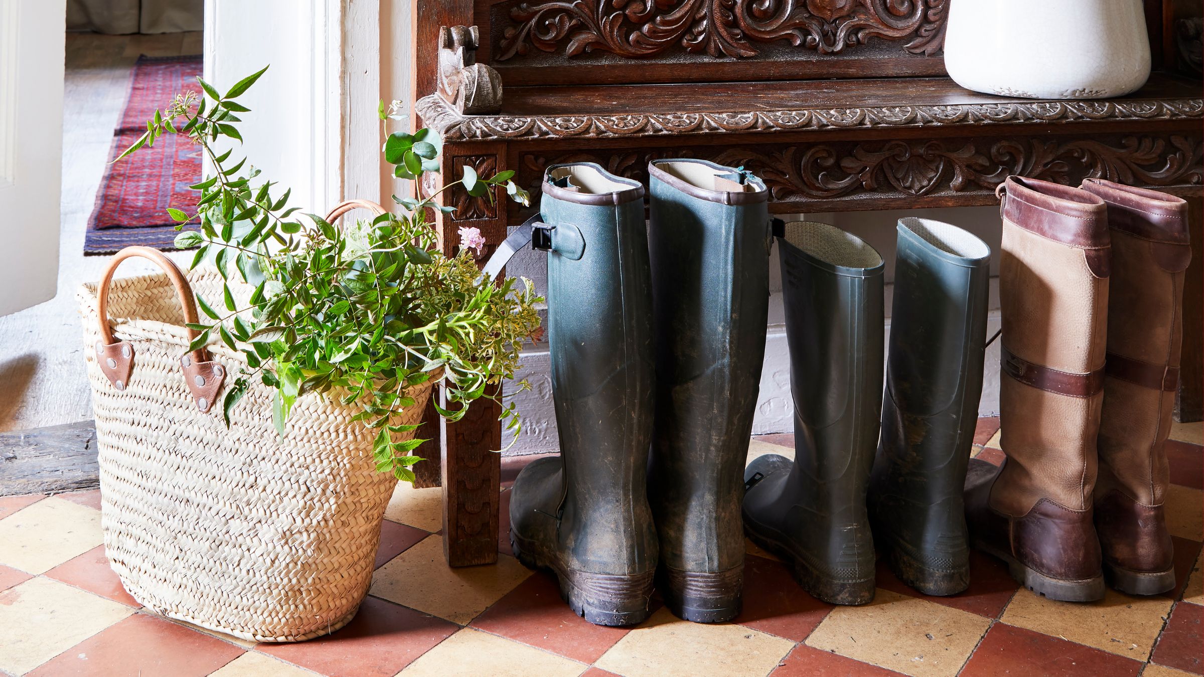 Wellington boots on checkerboard floor, with a wicker bag filled with plants next to them