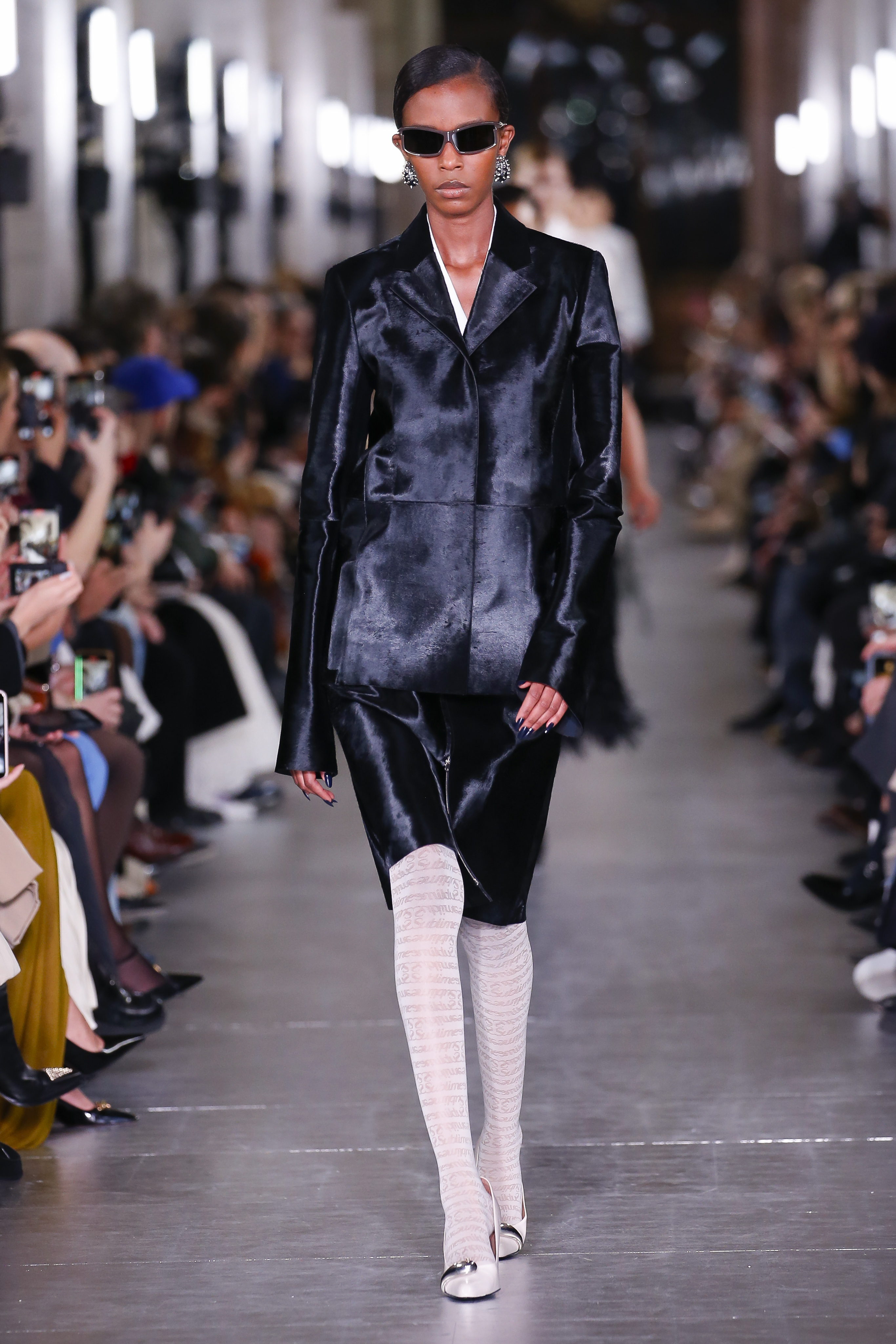 A Tory Burch model wearing a velvet black jacket and matching pencil skirt with white tights at the FW24 show.