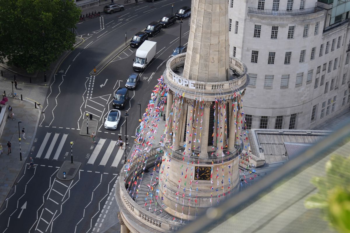 High-angle view of a London church tower decorated with colorful flags beside a busy road.