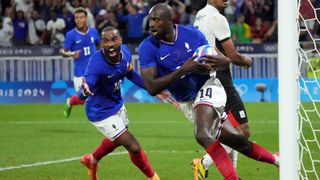 Jean-Philippe Mateta (R), in a blue shirt, white shorts and red socks, runs the ball back to the center sport after scoring a goal for France in a men&#039;s soccer match at the 2024 Paris Olympic Games.