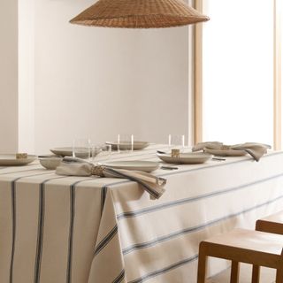 A dining table covered with a striped tablecloth and a rattan lampshade hanging above