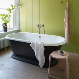 bathroom trends, bathroom with lime wall, colour drenching, black bath, pink stool, black and white vase, wooden floorboards