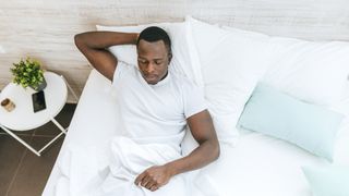 Man lies in bed with one hand behind his head