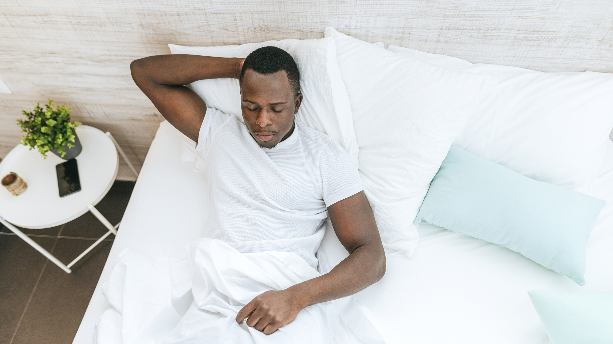 Man lies in bed with one hand behind his head