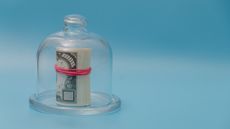 A rolled wad of cash under a glass dome against a blue background.