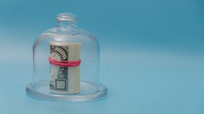 A rolled wad of cash under a glass dome against a blue background.