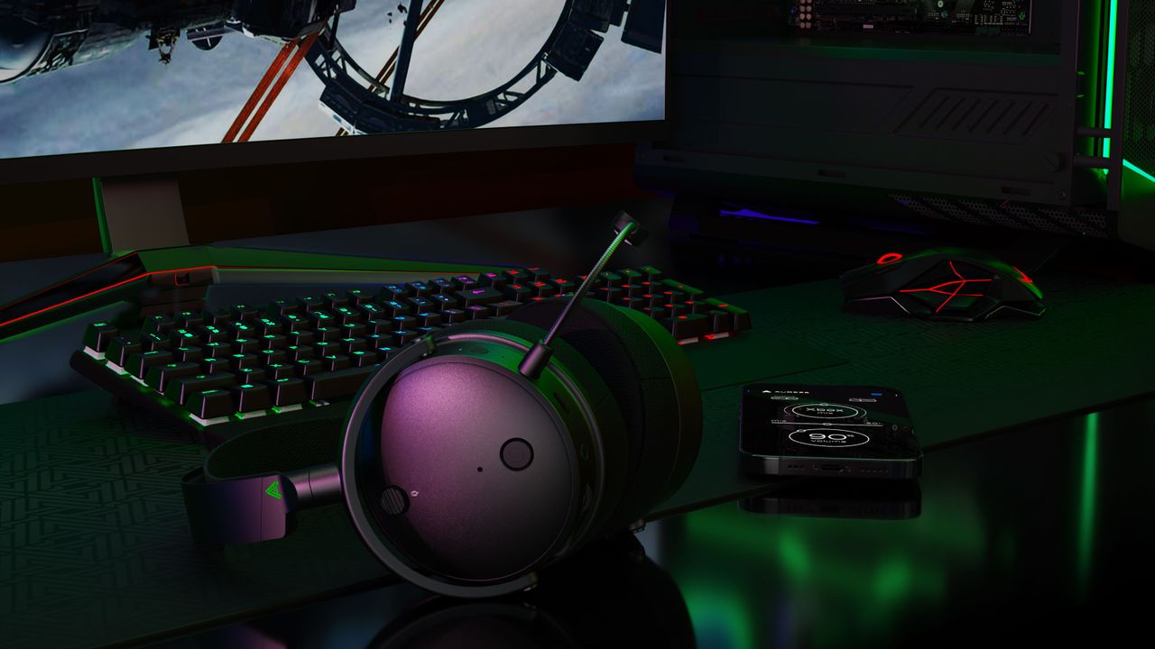 Audeze Maxwell wireless gaming headset for Xbox &amp; PC on a desk with keyboard, mouse, phone, and gaming desktop.