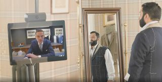 A man with a beard standing in front of a long mirror and trying on a suite.