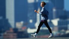 Woman walking with city skyline behind her. She is swinging her arms