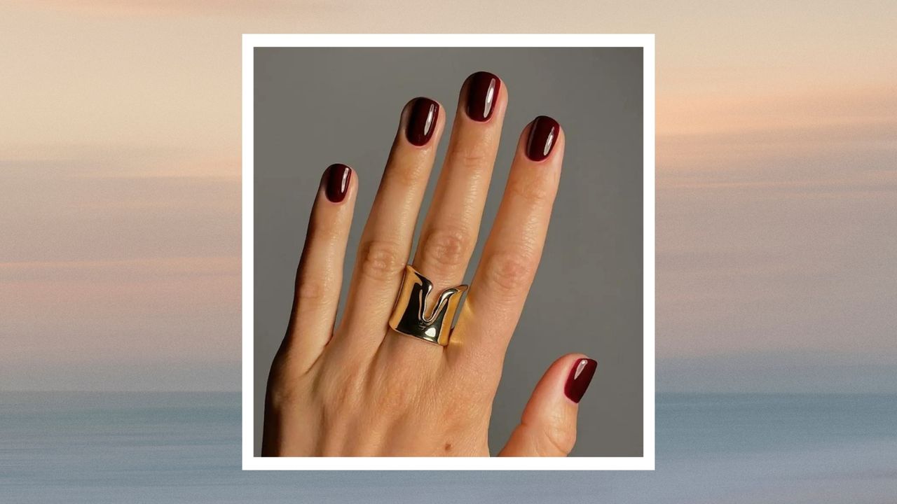 A close up of a hand with short burgundy dark nails by nail artist, @matejanova/ Mateja Novakovic | in a beige and blue sunset template