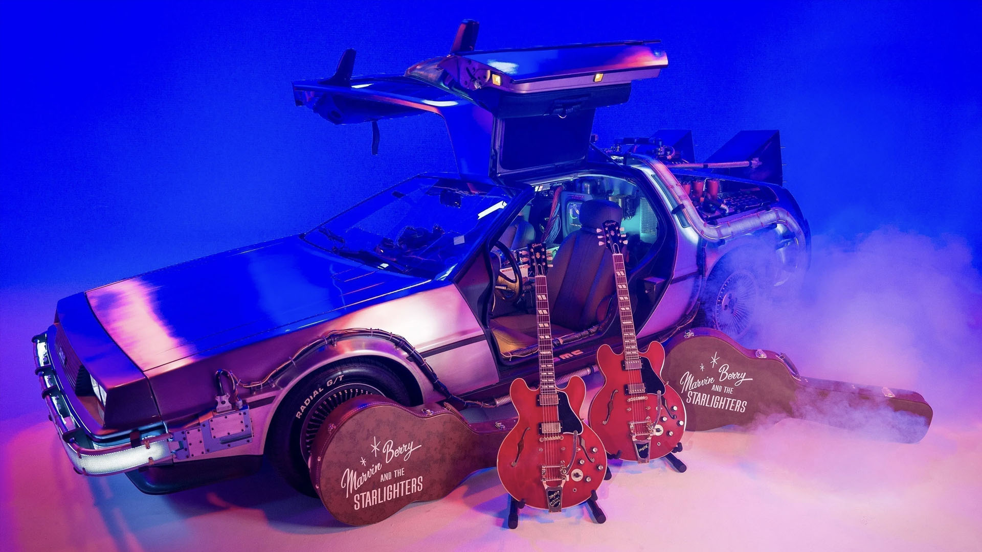 A photo of two Gibson guitars in front of a DeLorean car.