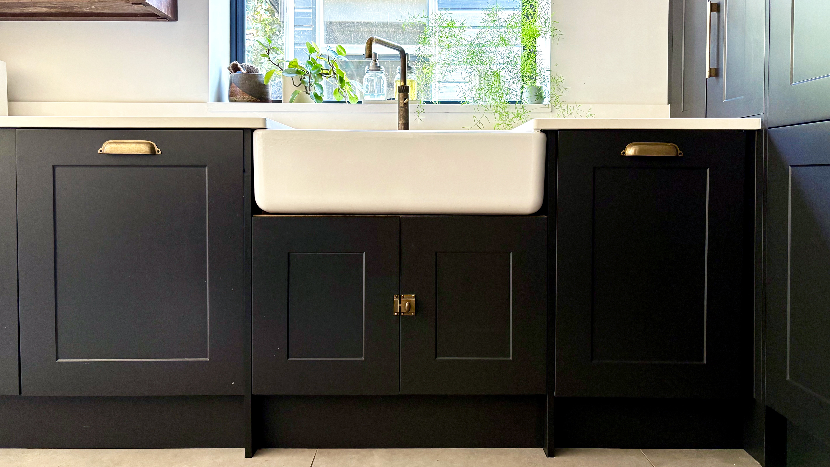 Dark grey kitchen base cabinets with brass handles and a white double belfast sink