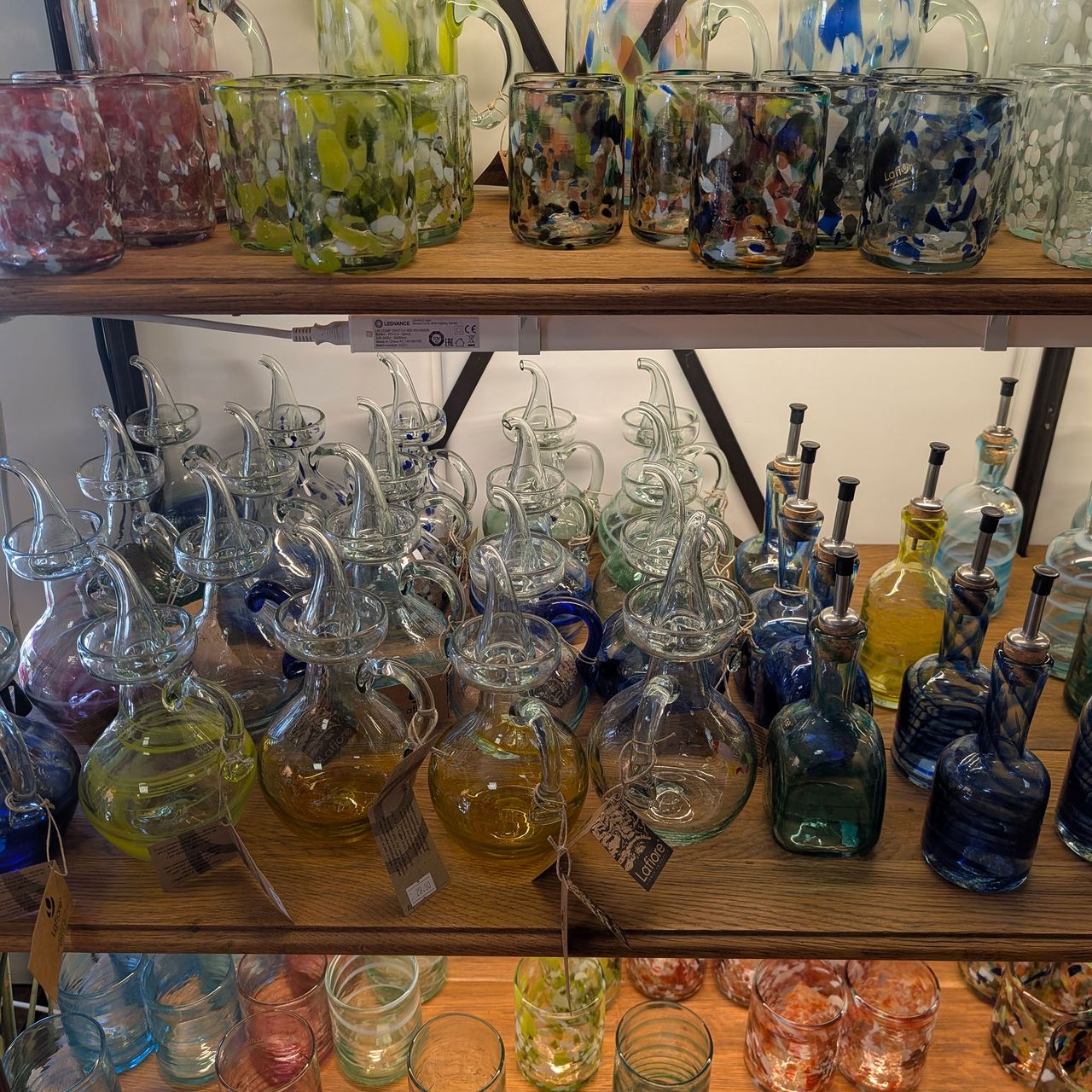Large selection of coloured glass jugs and glasses on wooden shelves